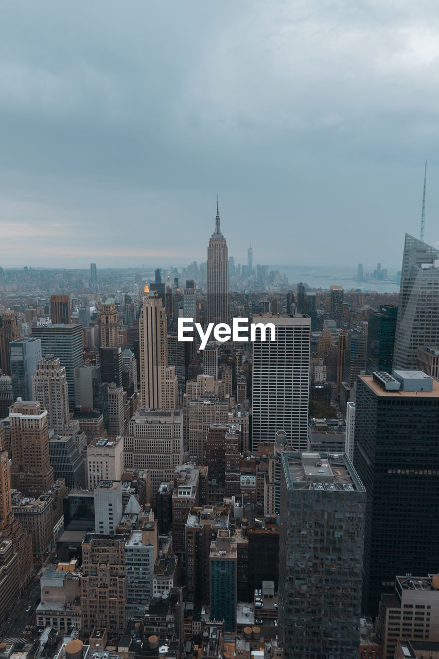 Aerial view of buildings in city against cloudy sky