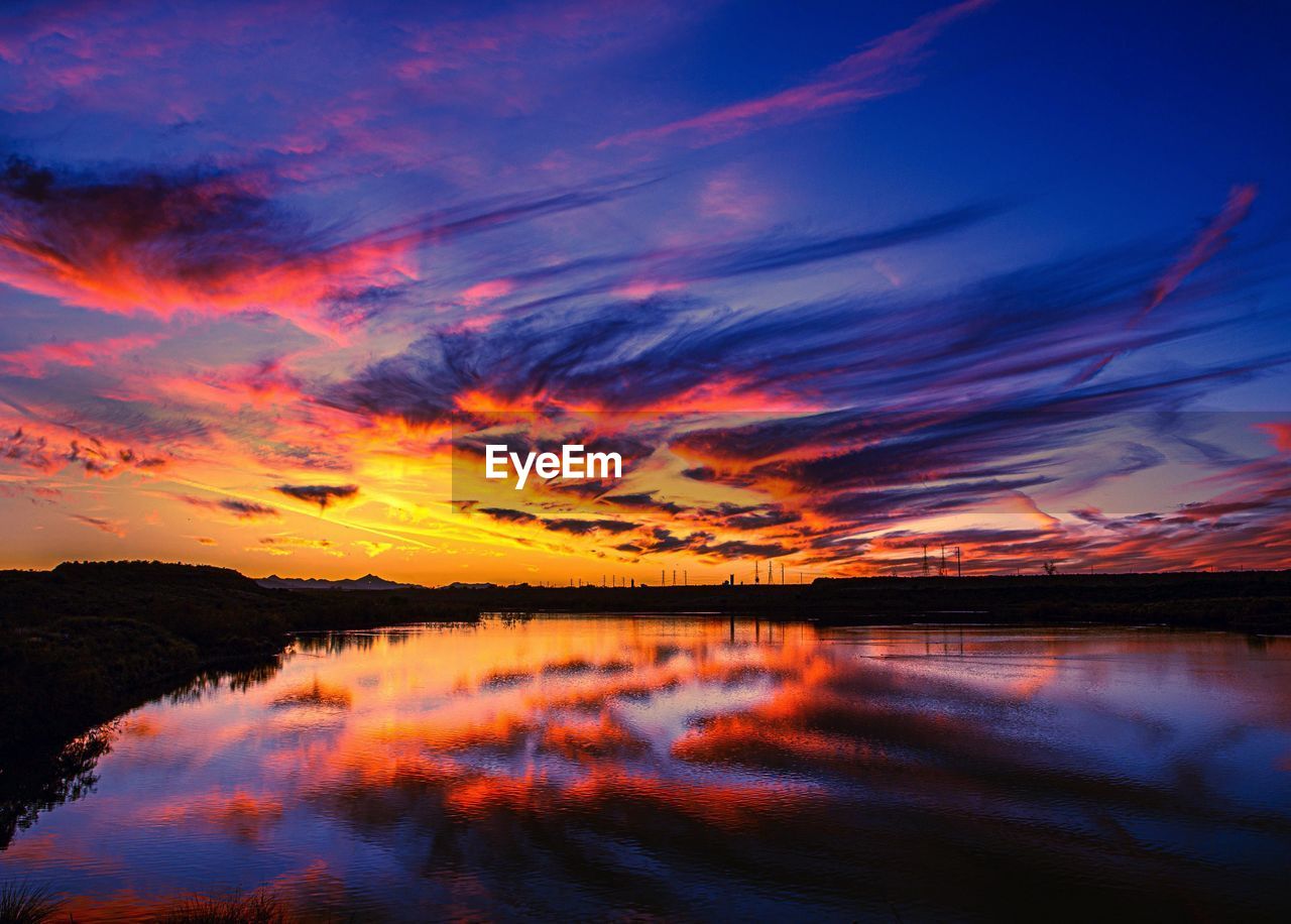 Scenic view of lake against dramatic sky during sunset