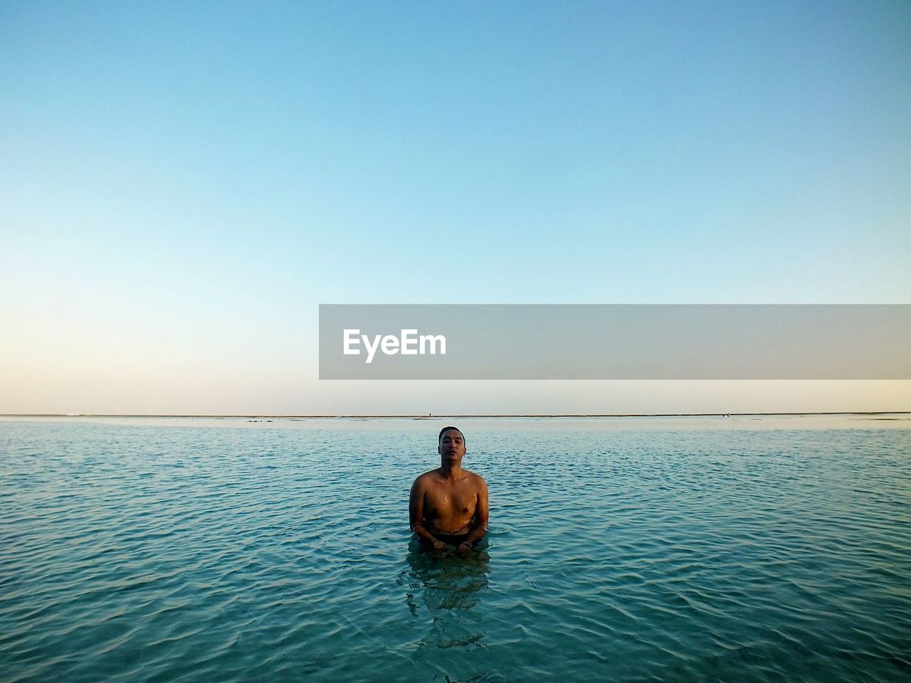 Portrait of shirtless mid adult man standing in sea against clear sky