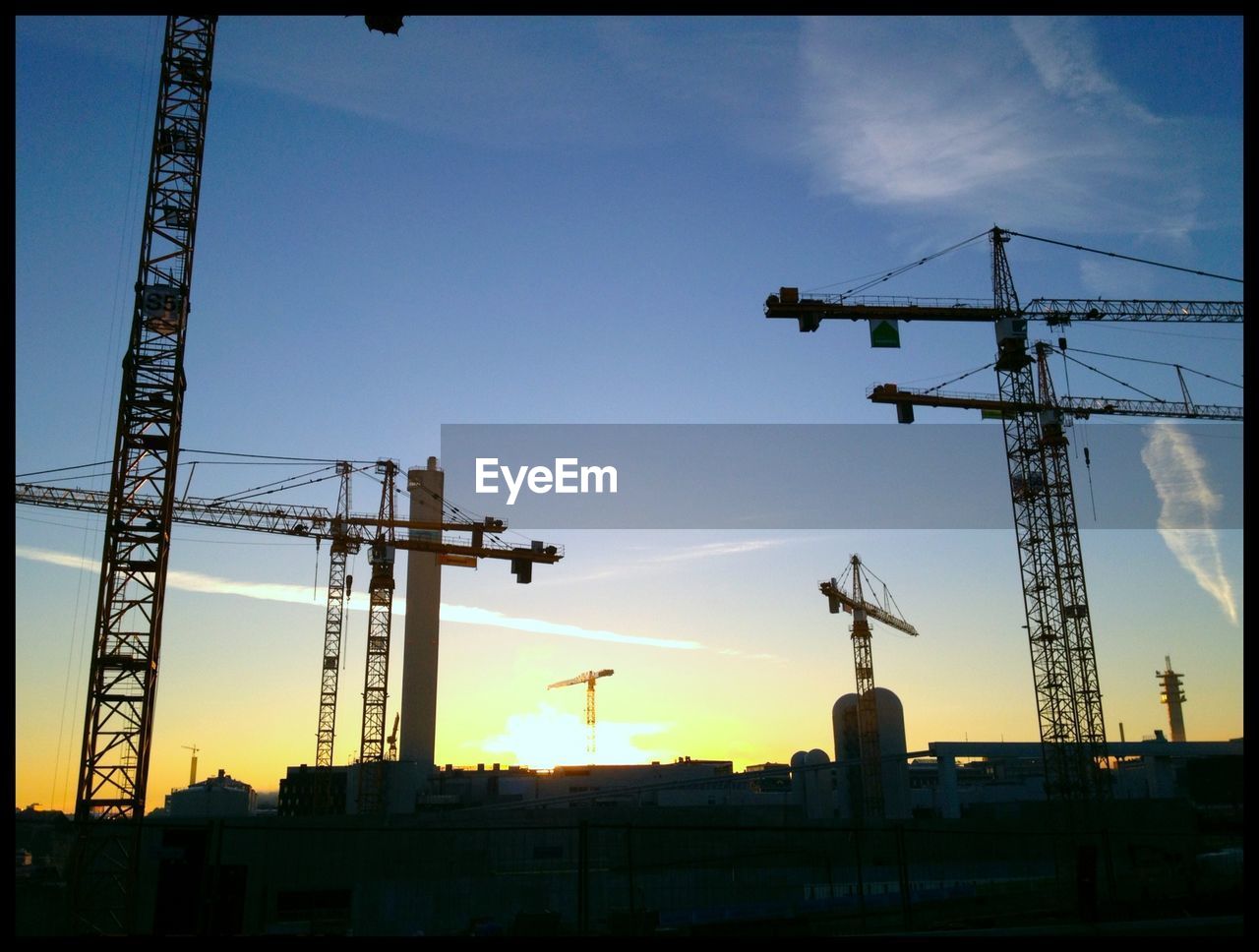 Low angle view of silhouette cranes at construction site during sunset