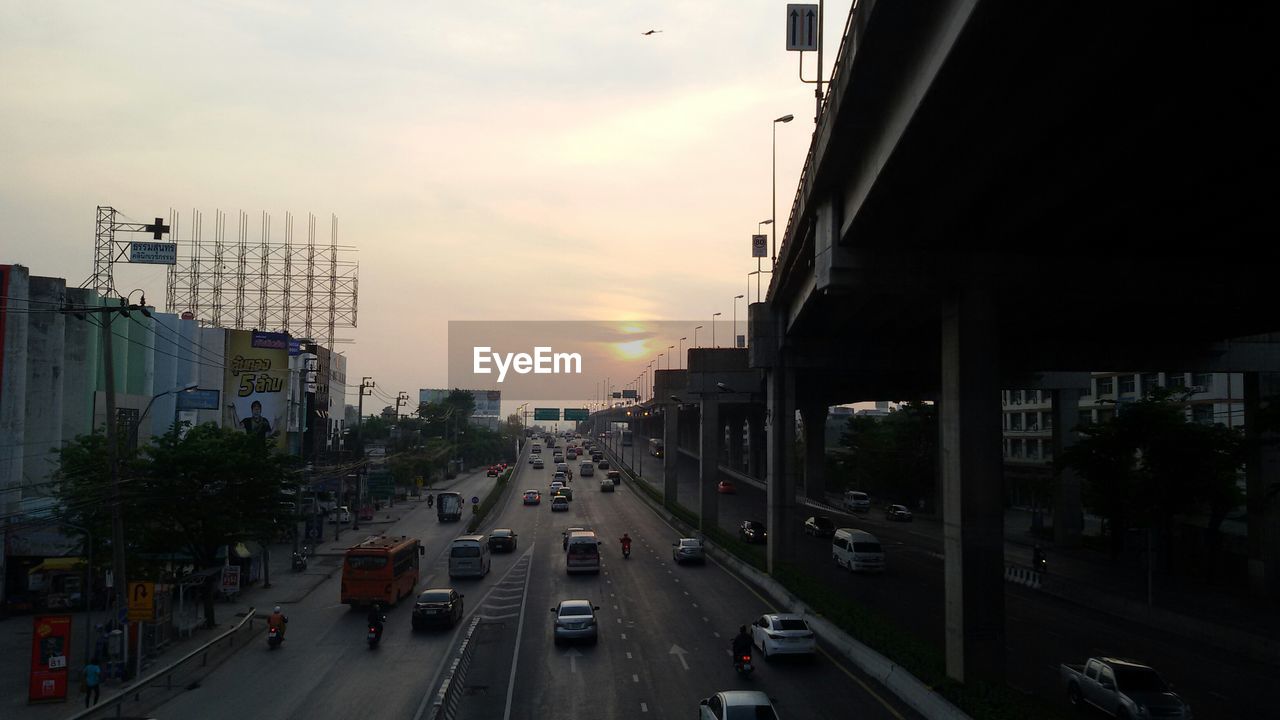 Vehicles on street by bridge in city during sunset