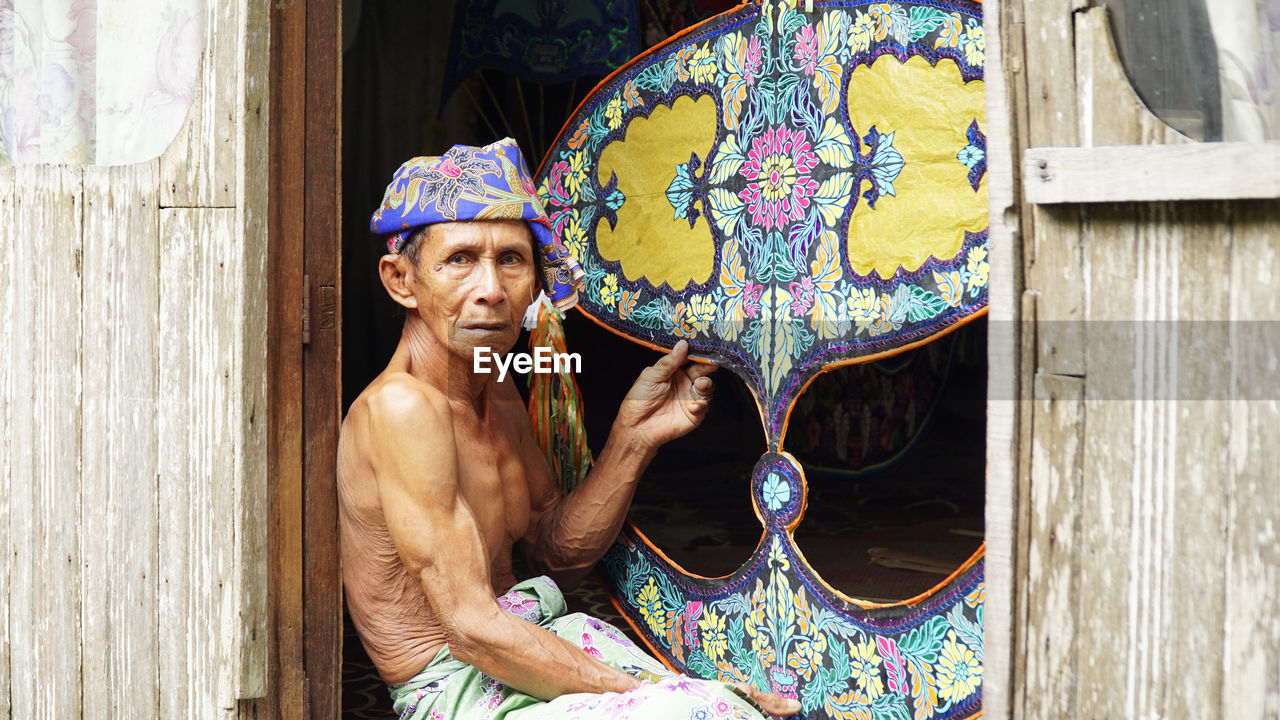 Portrait of shirtless man holding multi colored kite