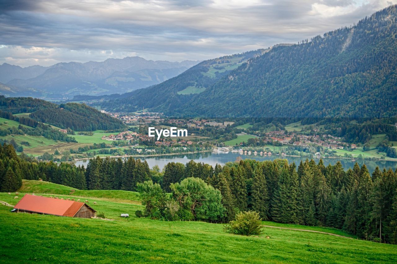 Scenic view of immenstadt by lake in valley against cloudy sky