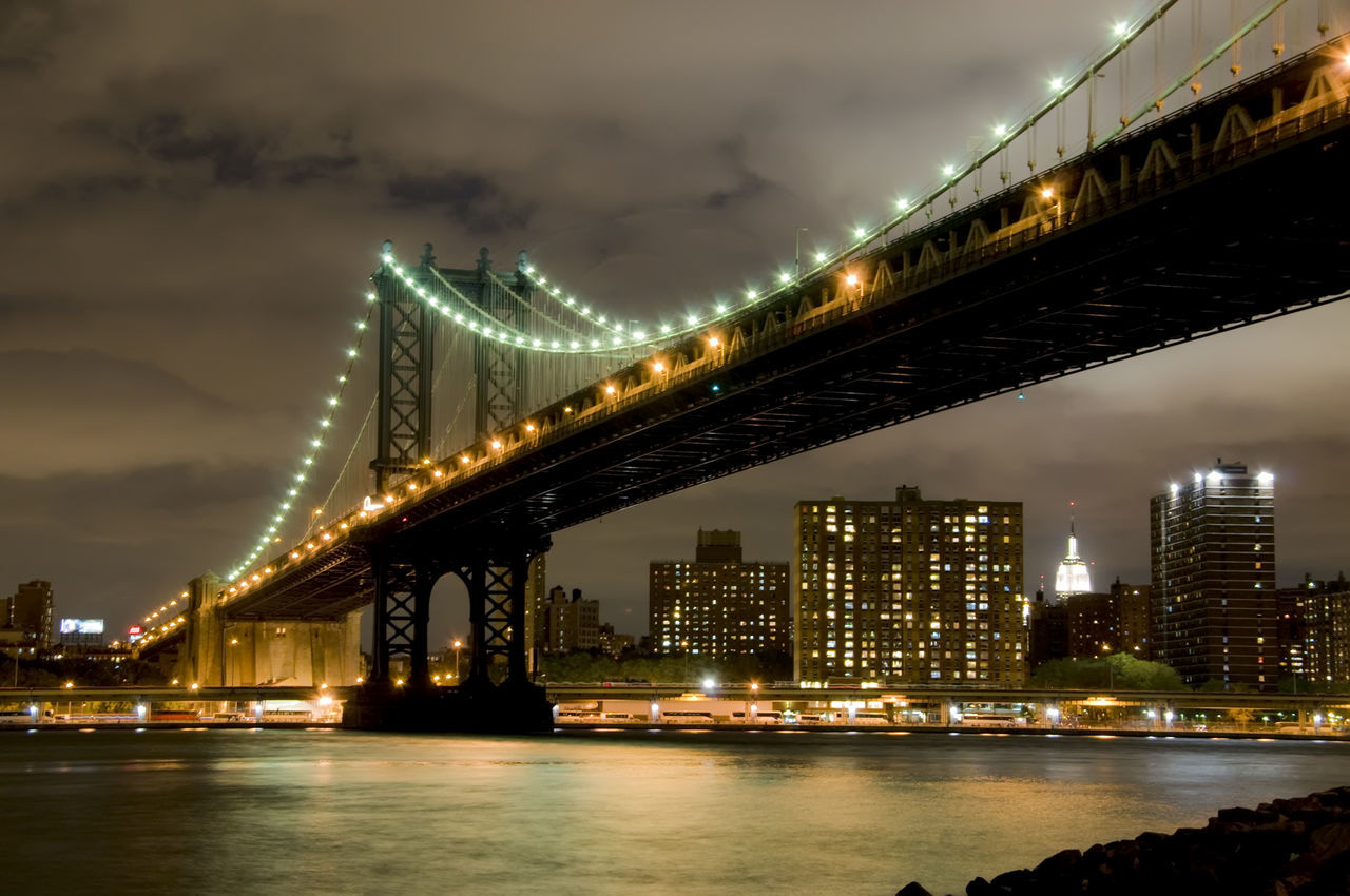 Manhattan bridge over river against cityscape at night