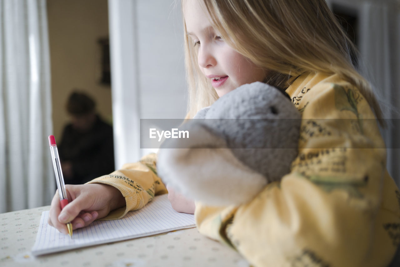 Midsection of girl writing in book at home