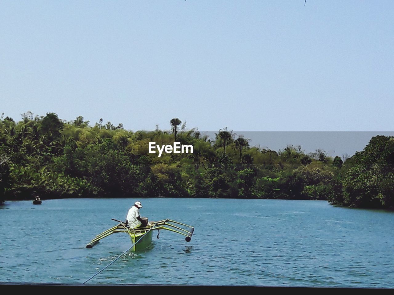 MAN SITTING IN BOAT SAILING ON RIVER AGAINST SKY