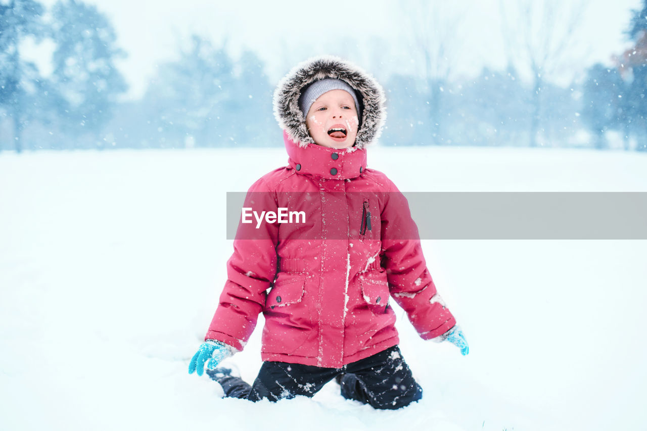 Caucasian excited girl child eating licking snow during cold winter snowy day. kids outdoor 