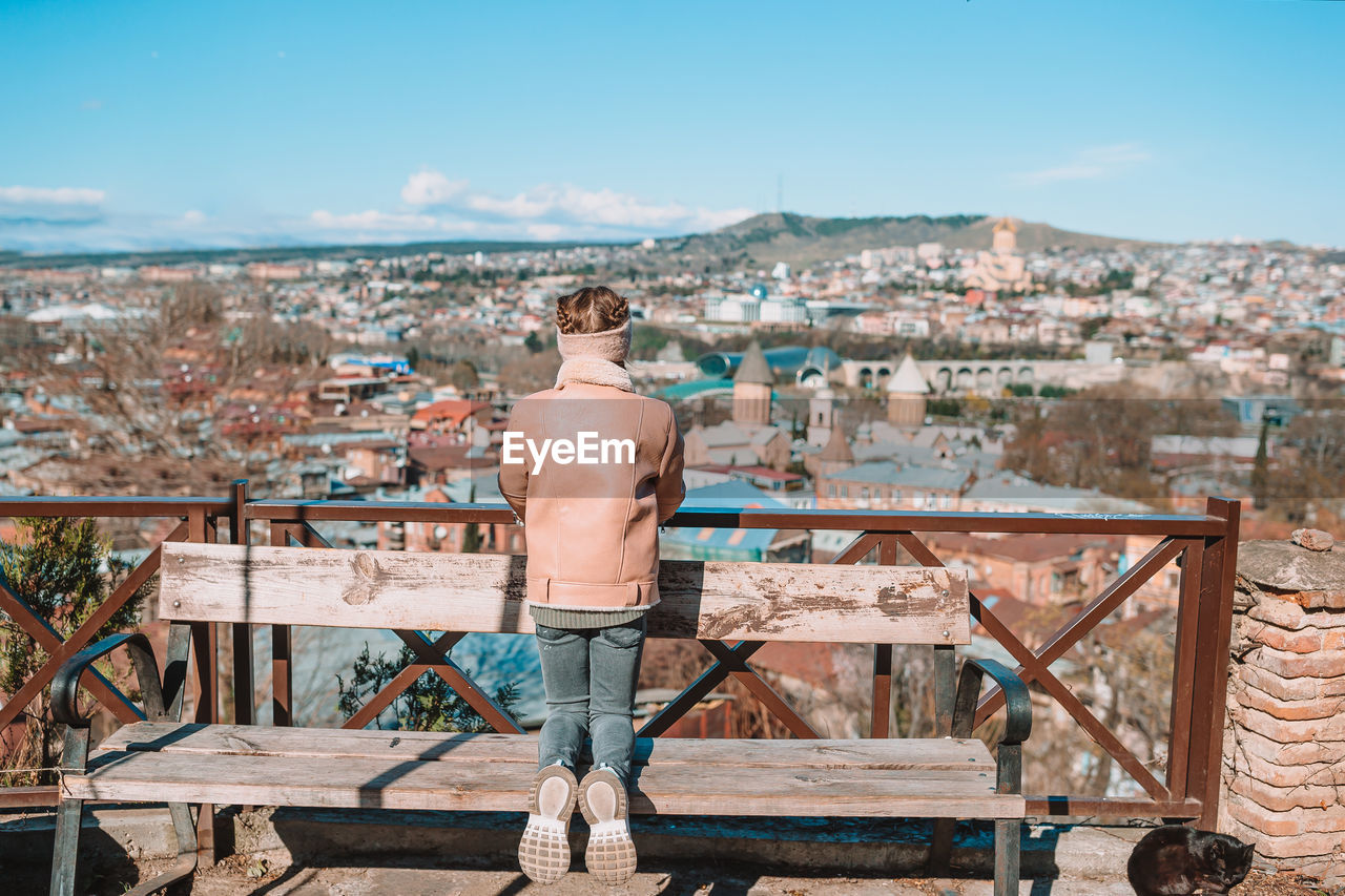 REAR VIEW OF SHIRTLESS MAN STANDING AGAINST BUILDINGS