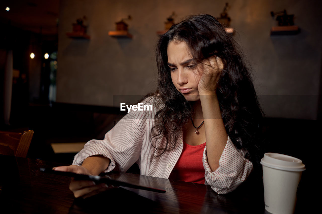 young woman using mobile phone while sitting on table at home