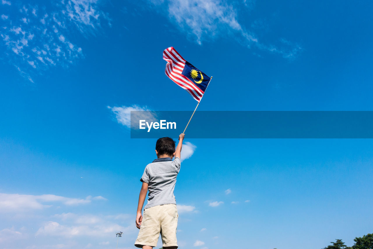 Low angle view of boy holding flag while standing against blue sky