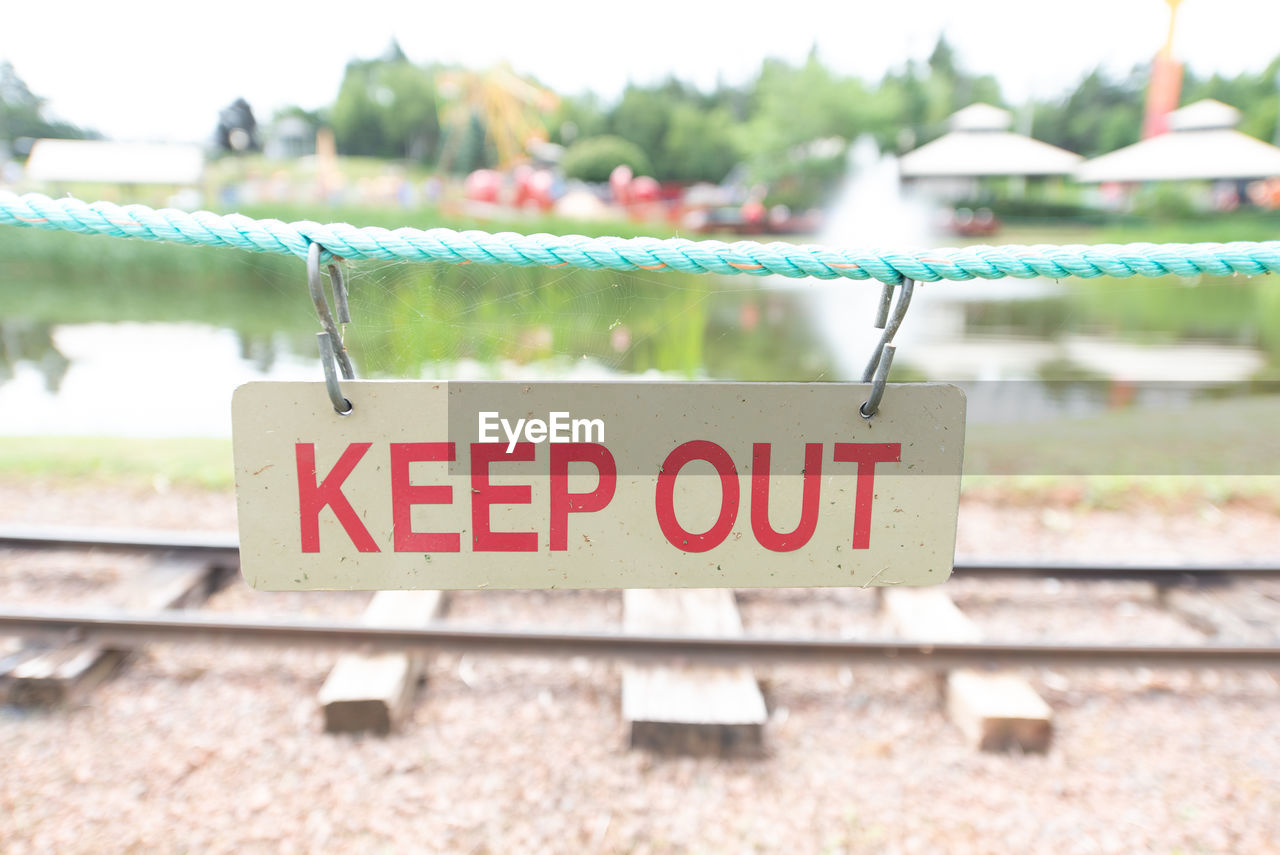 Close-up of keep out sign hanging on rope against railroad track