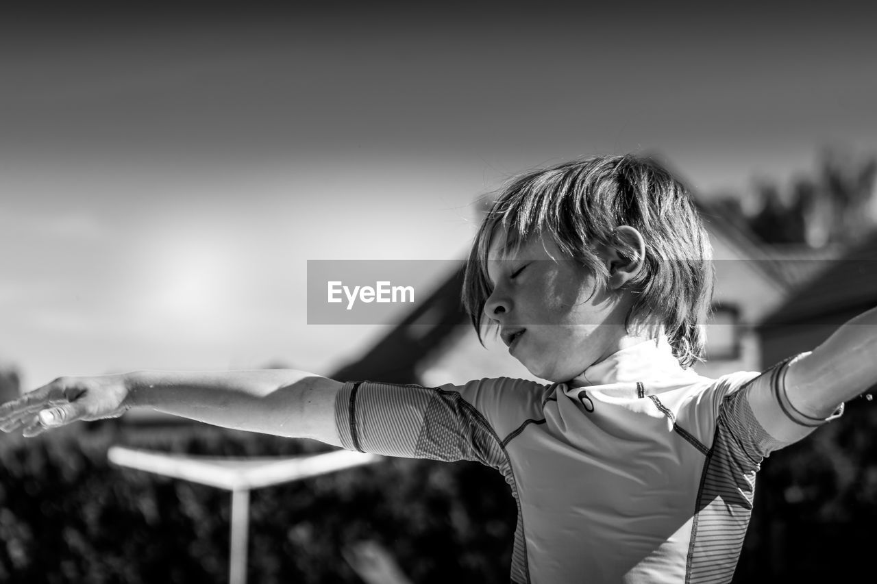 Rear view of boy with arms outstretched standing outdoors