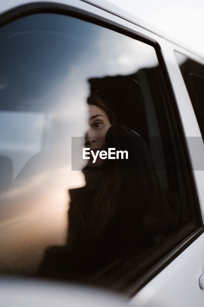 Young woman looks through a car window at sunset