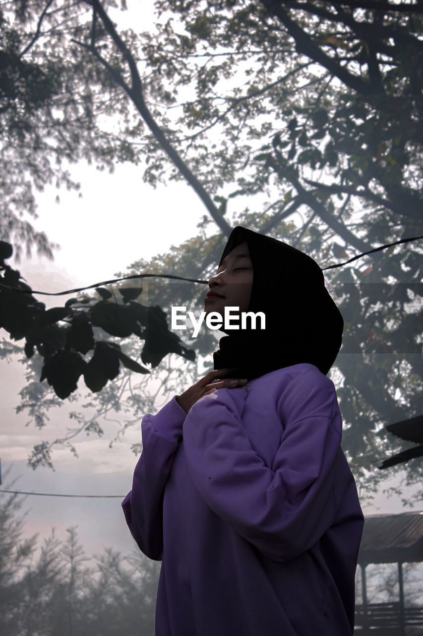 Woman standing by tree against sky during winter