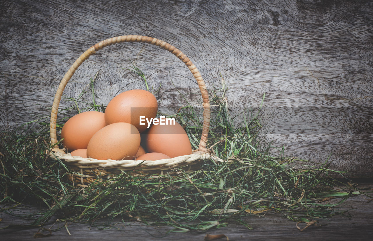 Close-up of eggs in wicker basket with grass by plant on table