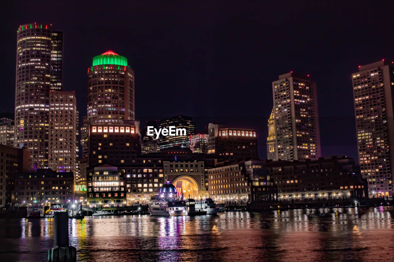 Illuminated buildings by river against sky at night