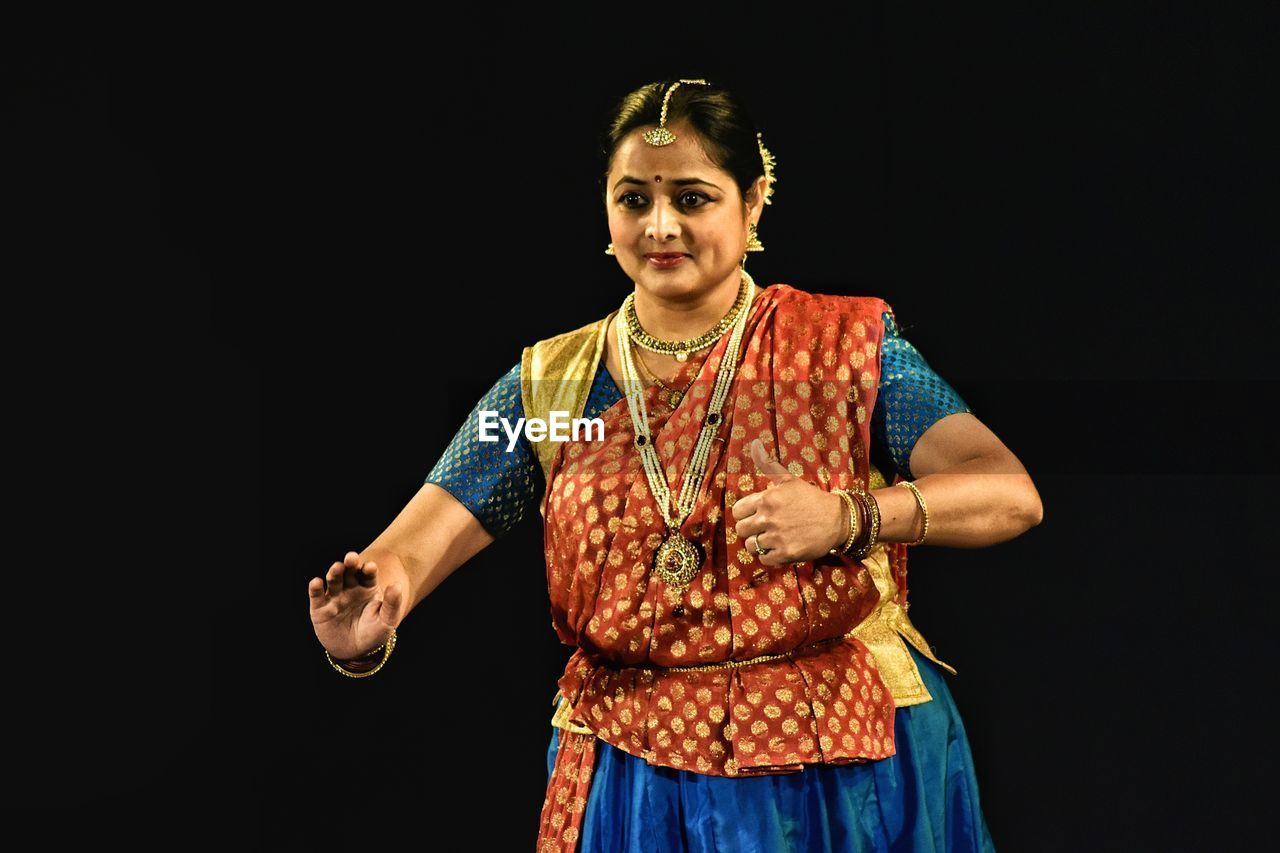 Smiling woman performing kathak against black background