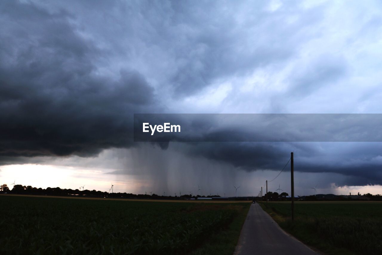 Road on field against storm clouds