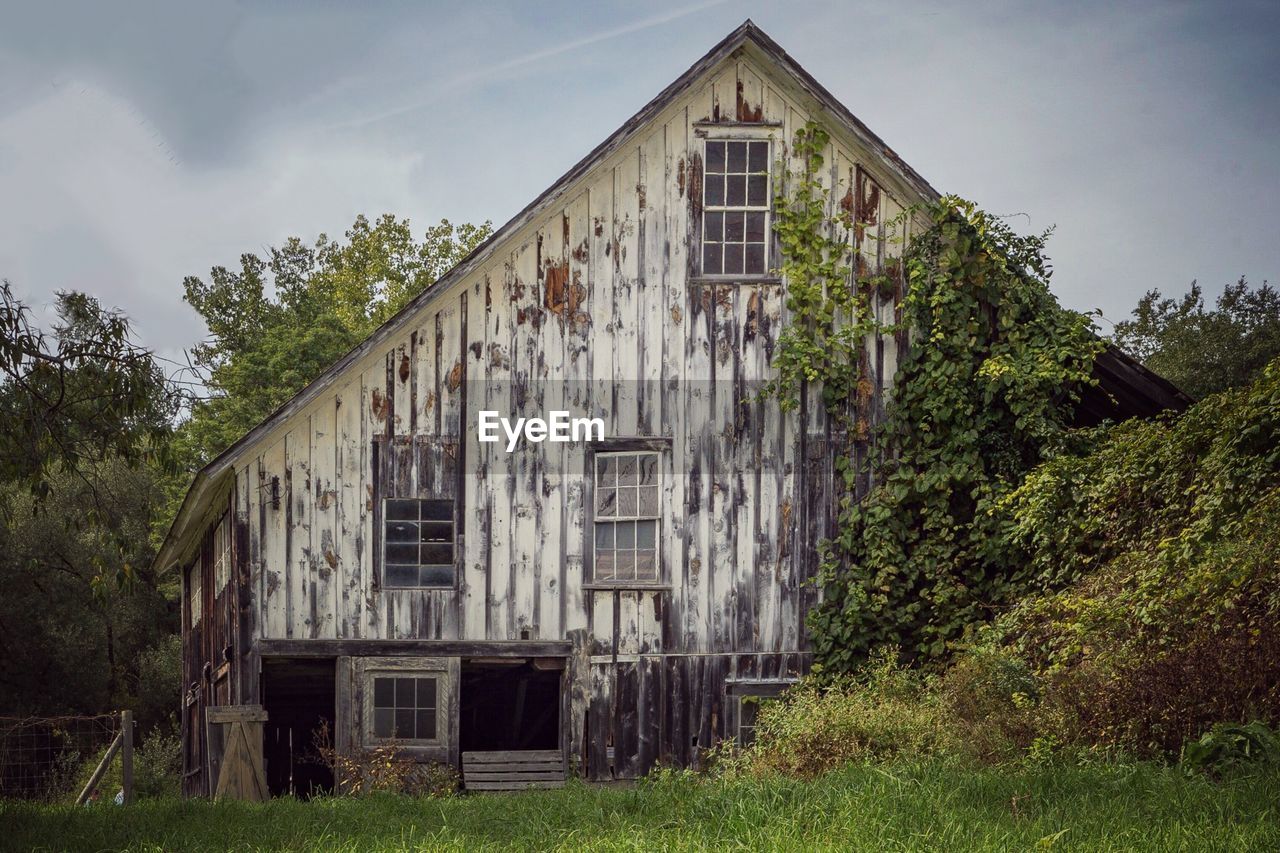 Exterior of abandoned house by trees against sky