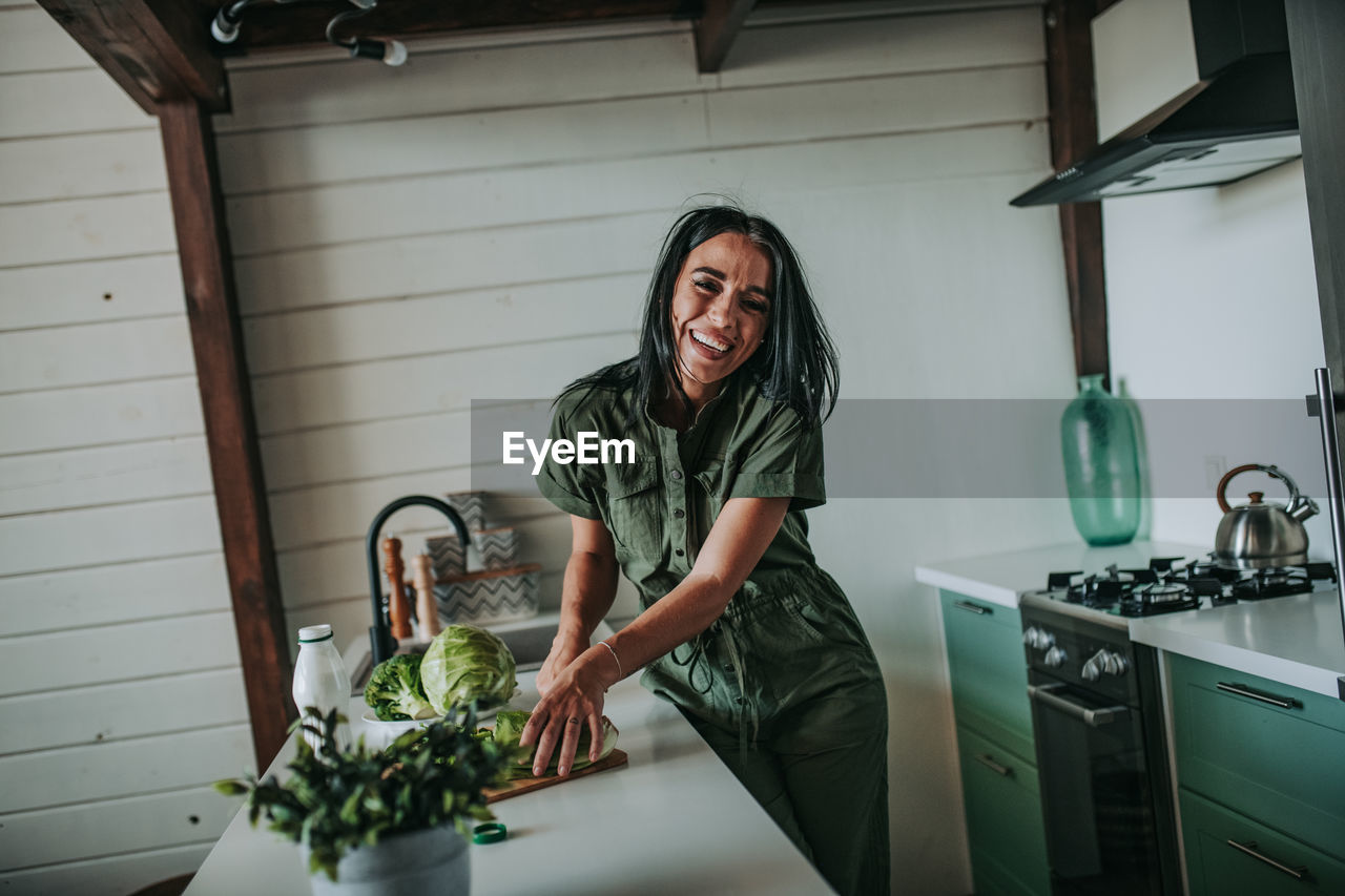 Portrait of woman holding cabbage while standing at kitchen