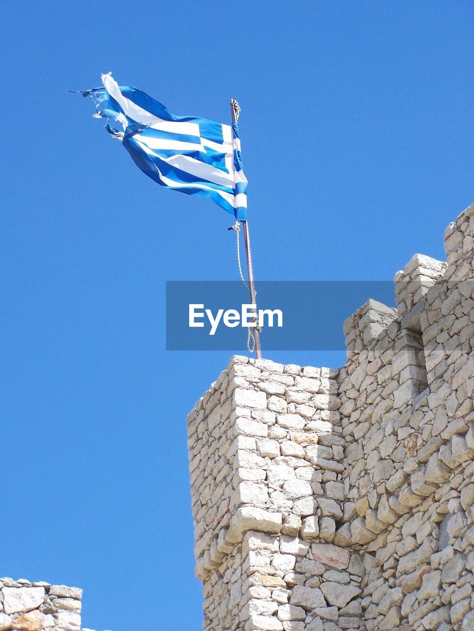 Low angle view of greek flag waving on fort against clear blue sky