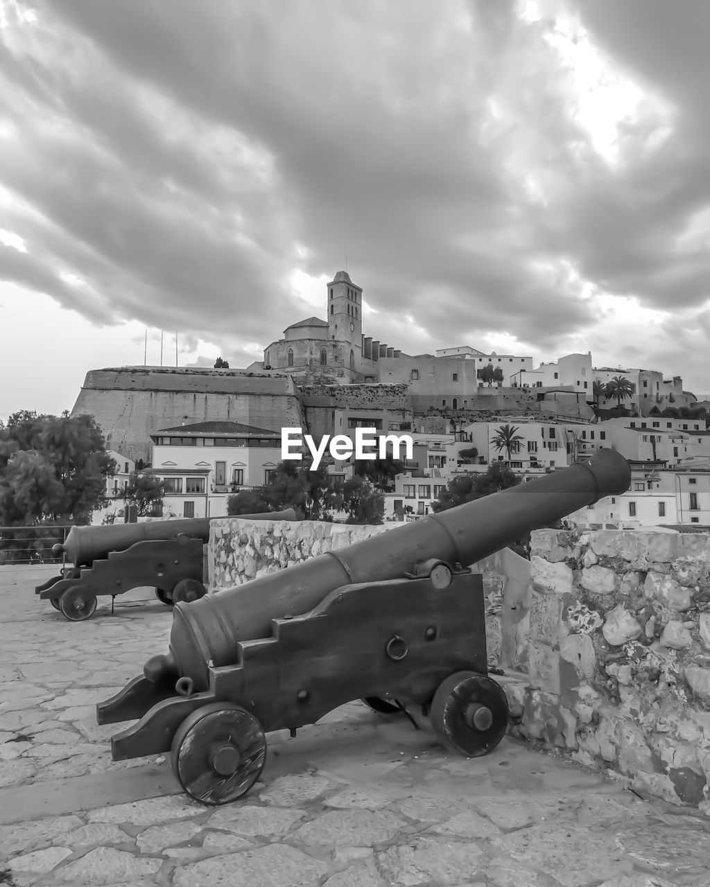 Cannons by historic building in town against cloudy sky