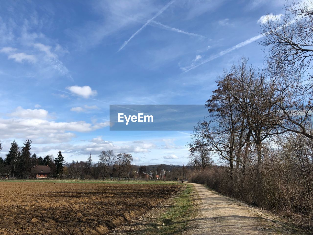 Dirt road amidst agricultural field against sky