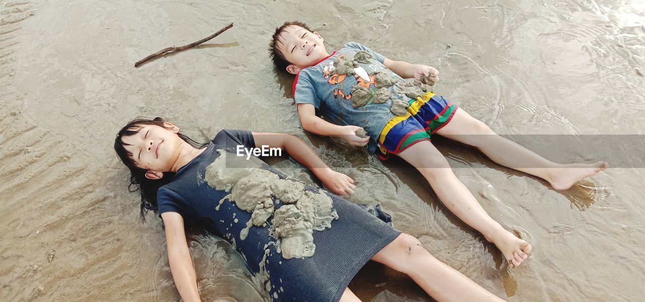 High angle view of siblings lying on beach