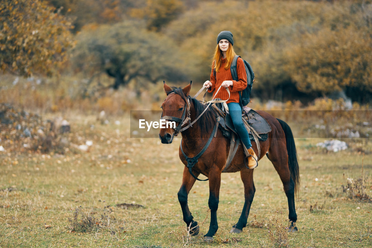 FULL LENGTH OF WOMAN RIDING HORSE ON FIELD