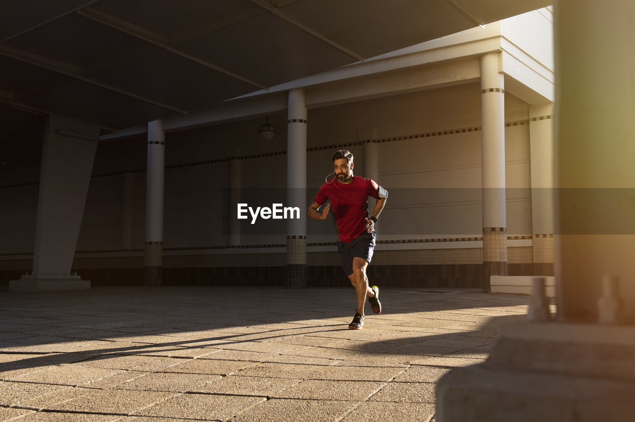 Full length of confident man running on footpath against building in city