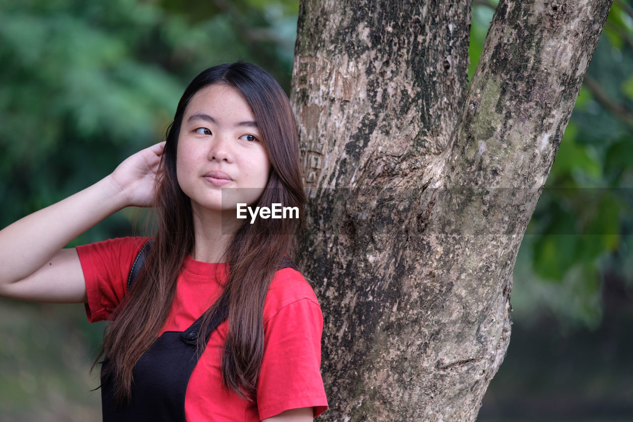 Young woman standing by tree trunk at park