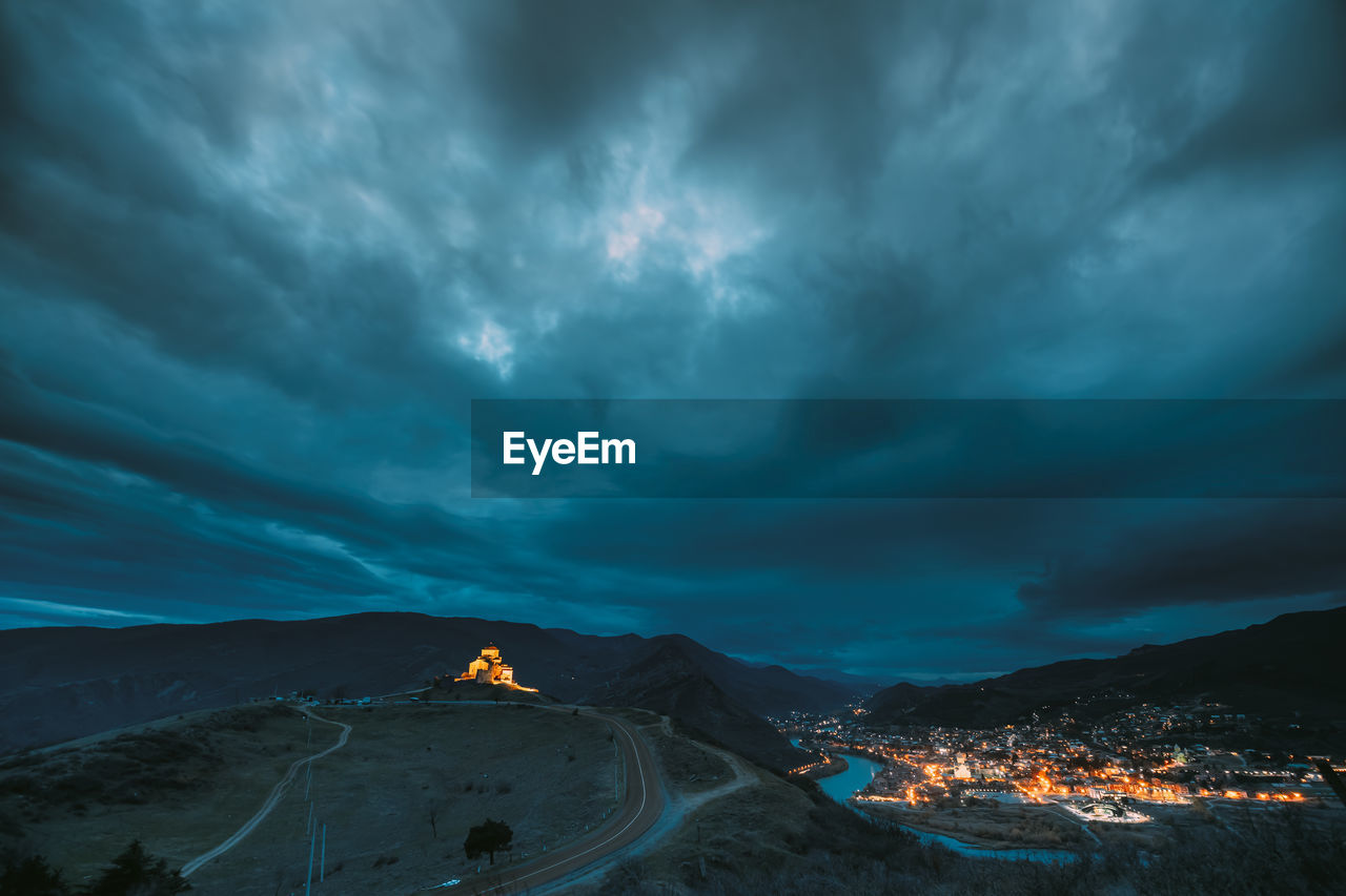 Aerial view of illuminated town by mountain against sky