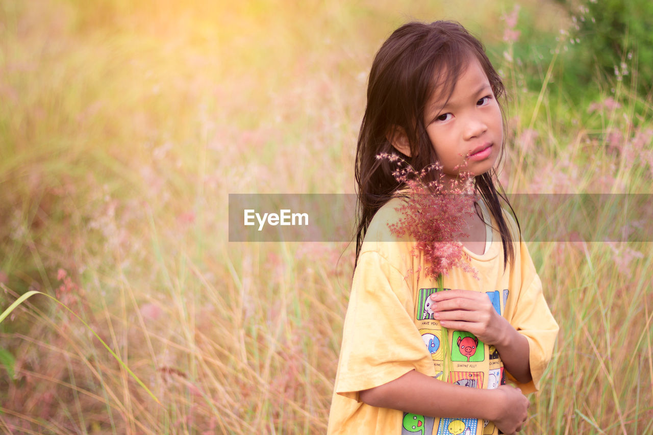 Portrait of girl holding plant while standing on grass