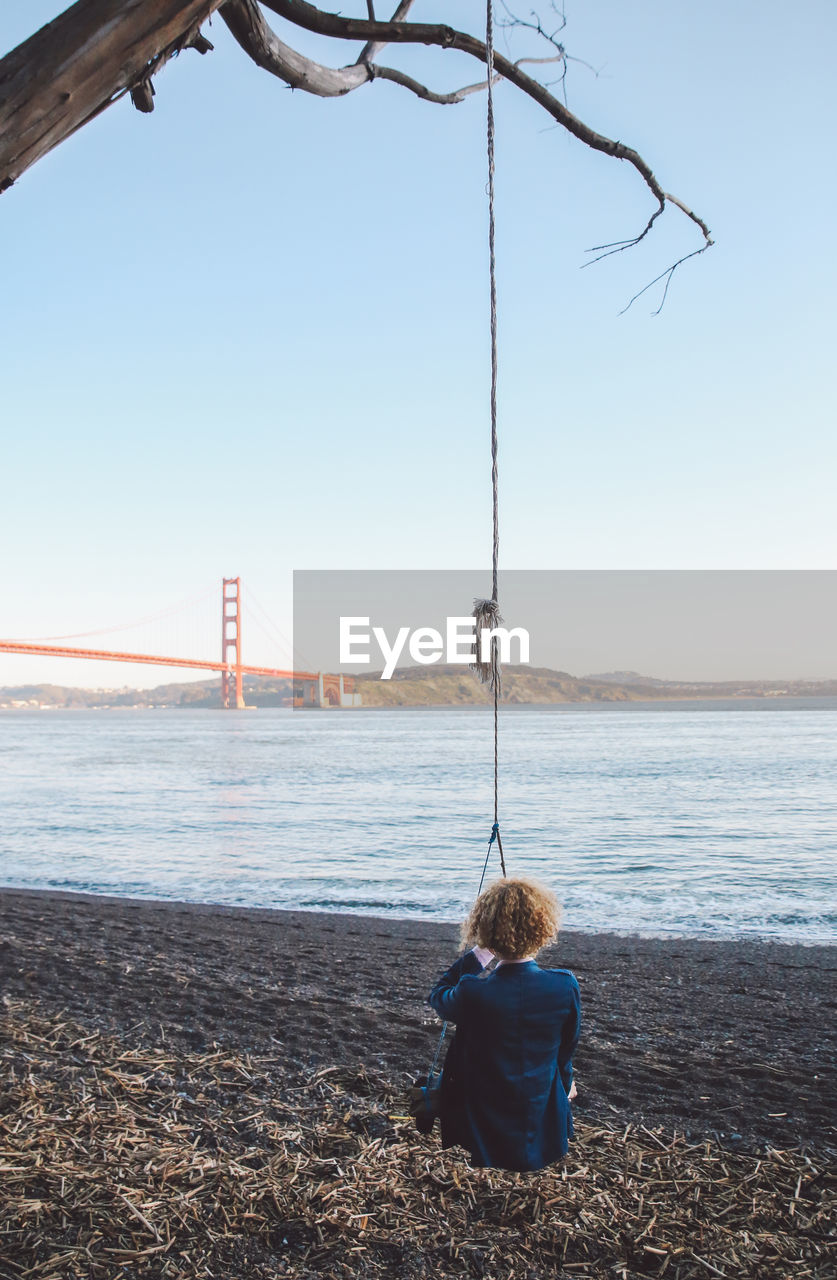 Rear view of woman sitting on swing with golden gate bridge in background