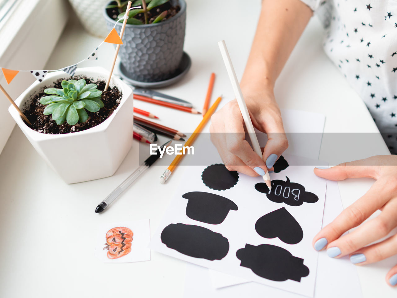 Woman writes boo on decorative black stickers for flower pots. handmade halloween decorations.