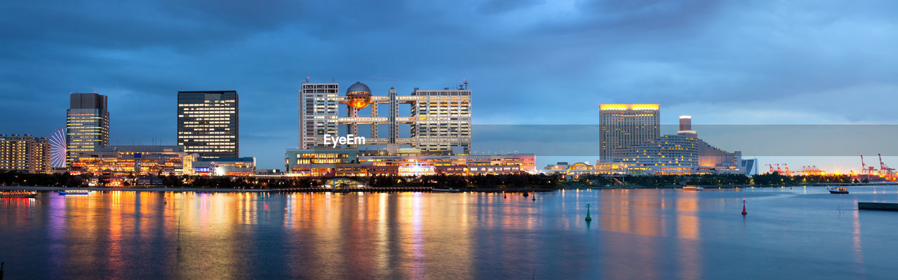 Illuminated city by river against sky