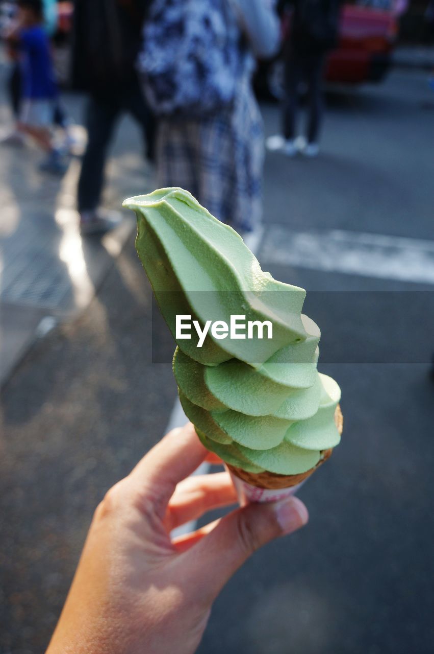 Cropped hand holding ice cream cone on street