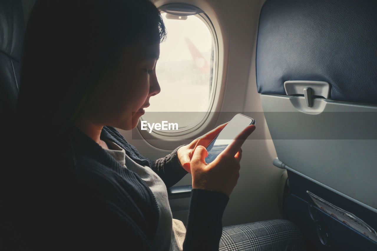 Young woman using mobile phone while sitting in airplane