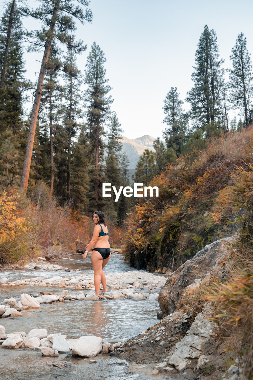 Woman walks along a creek in nature looking for the best thermal hot spring pool to sit back in 