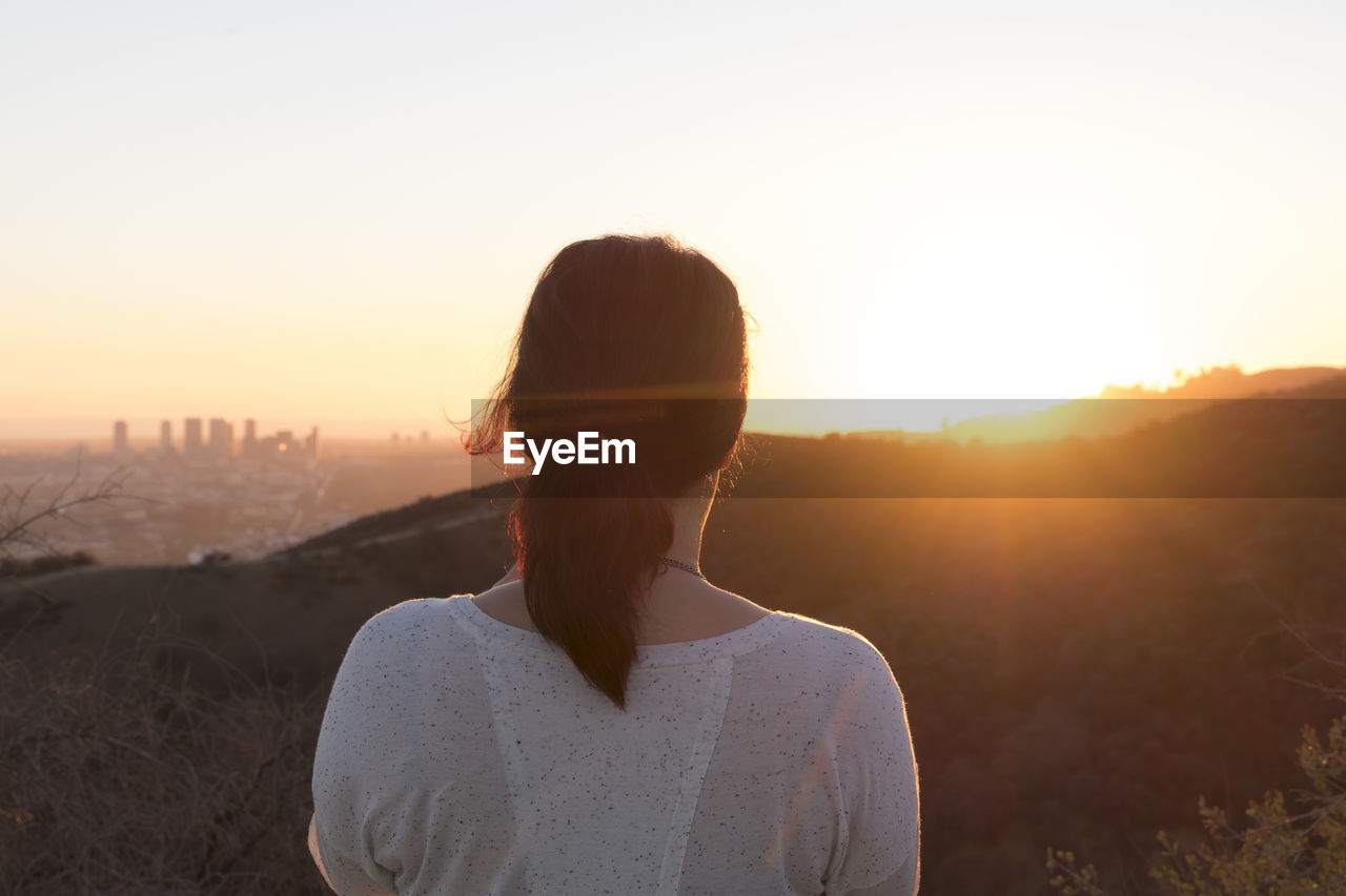 Rear view of woman looking at mountains against sky during sunset