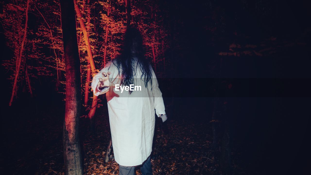 MIDSECTION OF WOMAN STANDING BY TREES IN FOREST