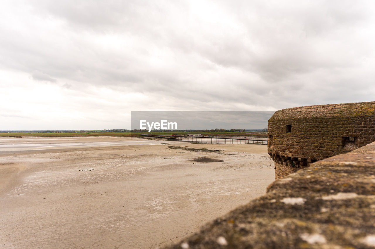sky, land, sea, coast, cloud, water, shore, beach, nature, sand, environment, scenics - nature, landscape, ocean, travel destinations, architecture, travel, beauty in nature, coastline, no people, overcast, wave, built structure, tranquility, outdoors, tourism, rock, day, horizon, body of water, water's edge, tranquil scene, dramatic sky, history, cloudscape, non-urban scene, trip