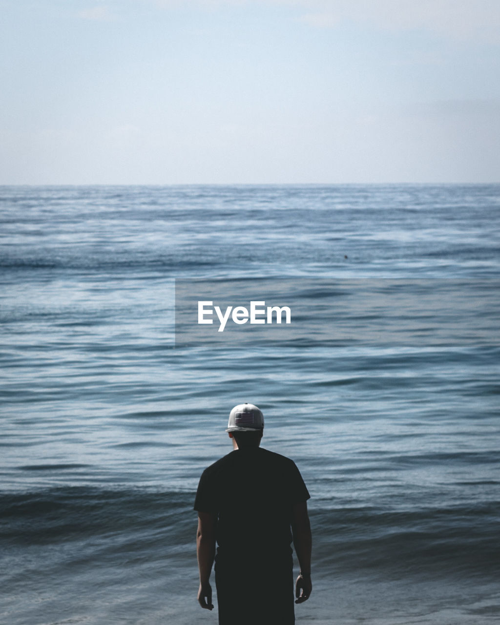 Rear view of man standing in sea against sky