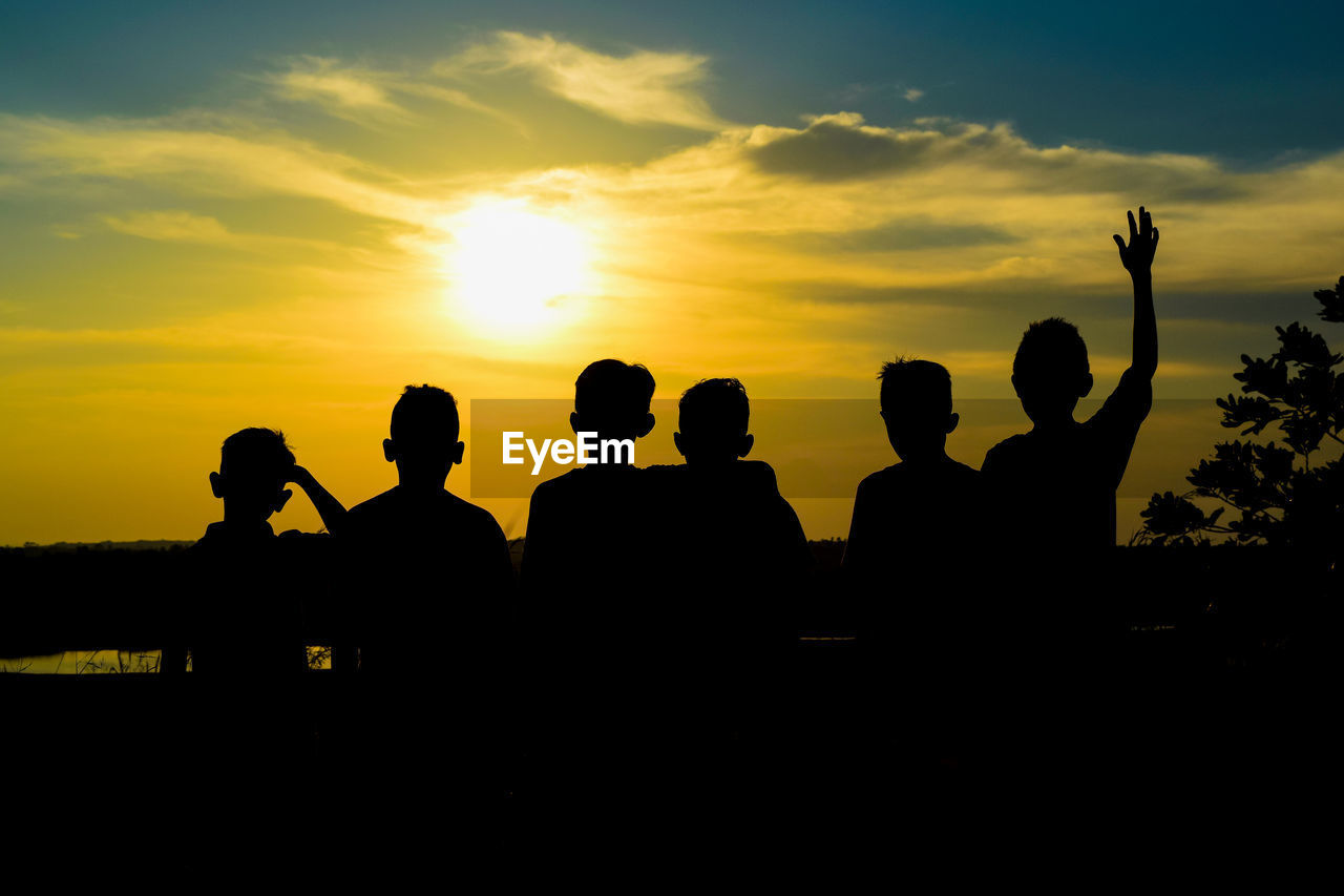 Rear view of silhouette boys standing against sky during sunset