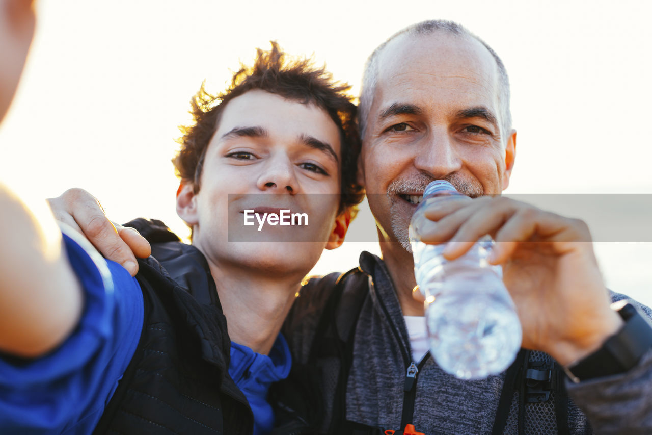 Close-up portrait of happy father and son against sky