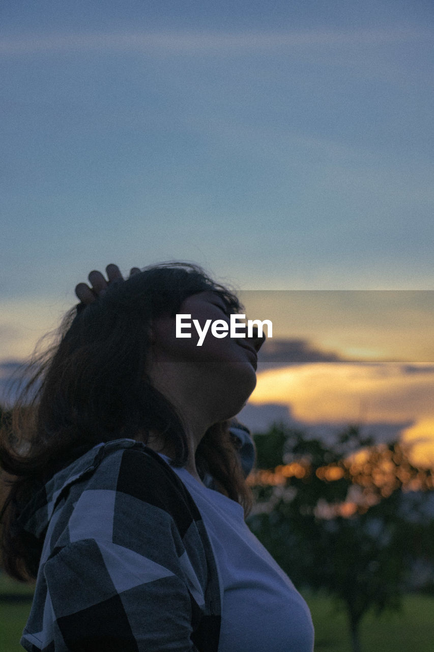 Young woman stretching against sky during sunset