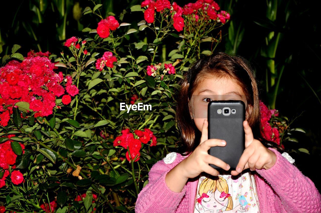 Girl photographing by flowers from mobile phone