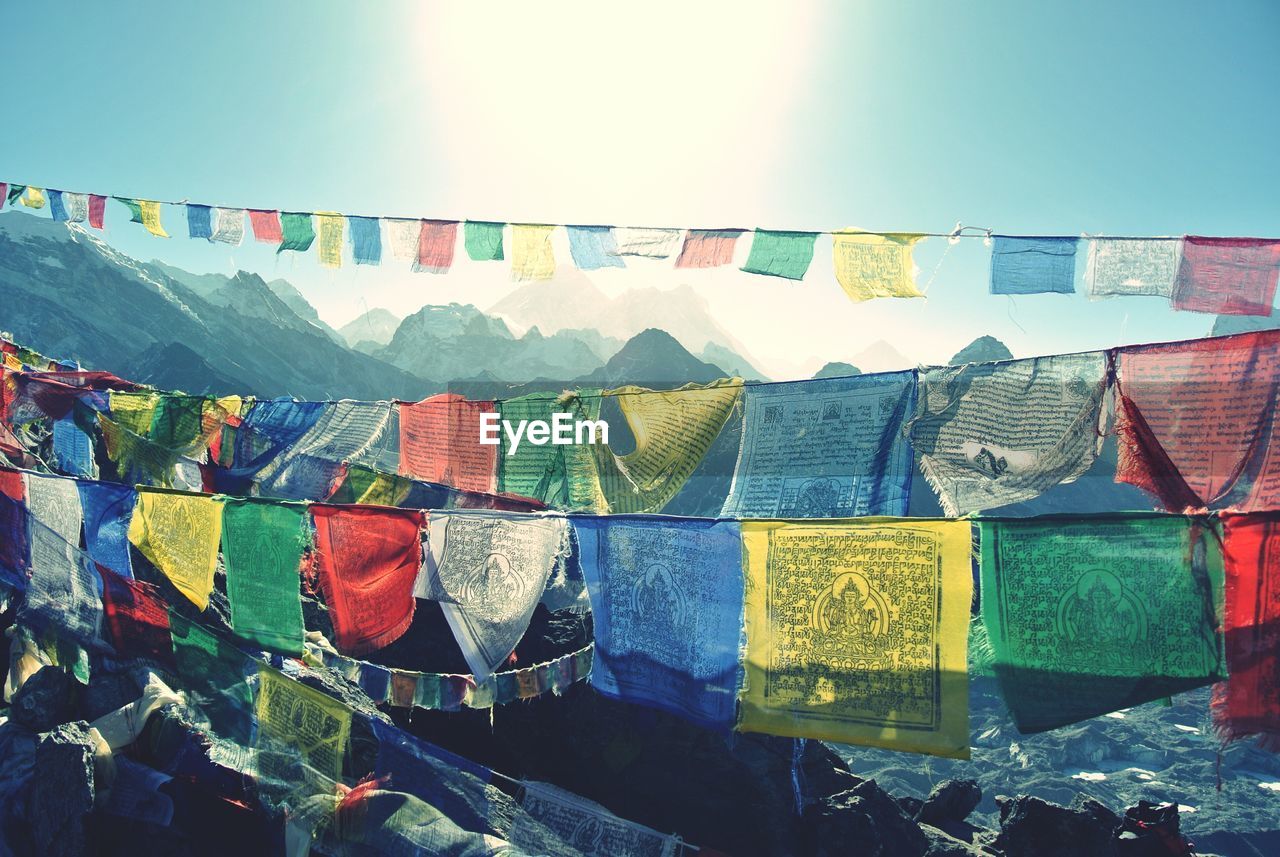 Colorful prayer flags hanging by mountains against sky on sunny day