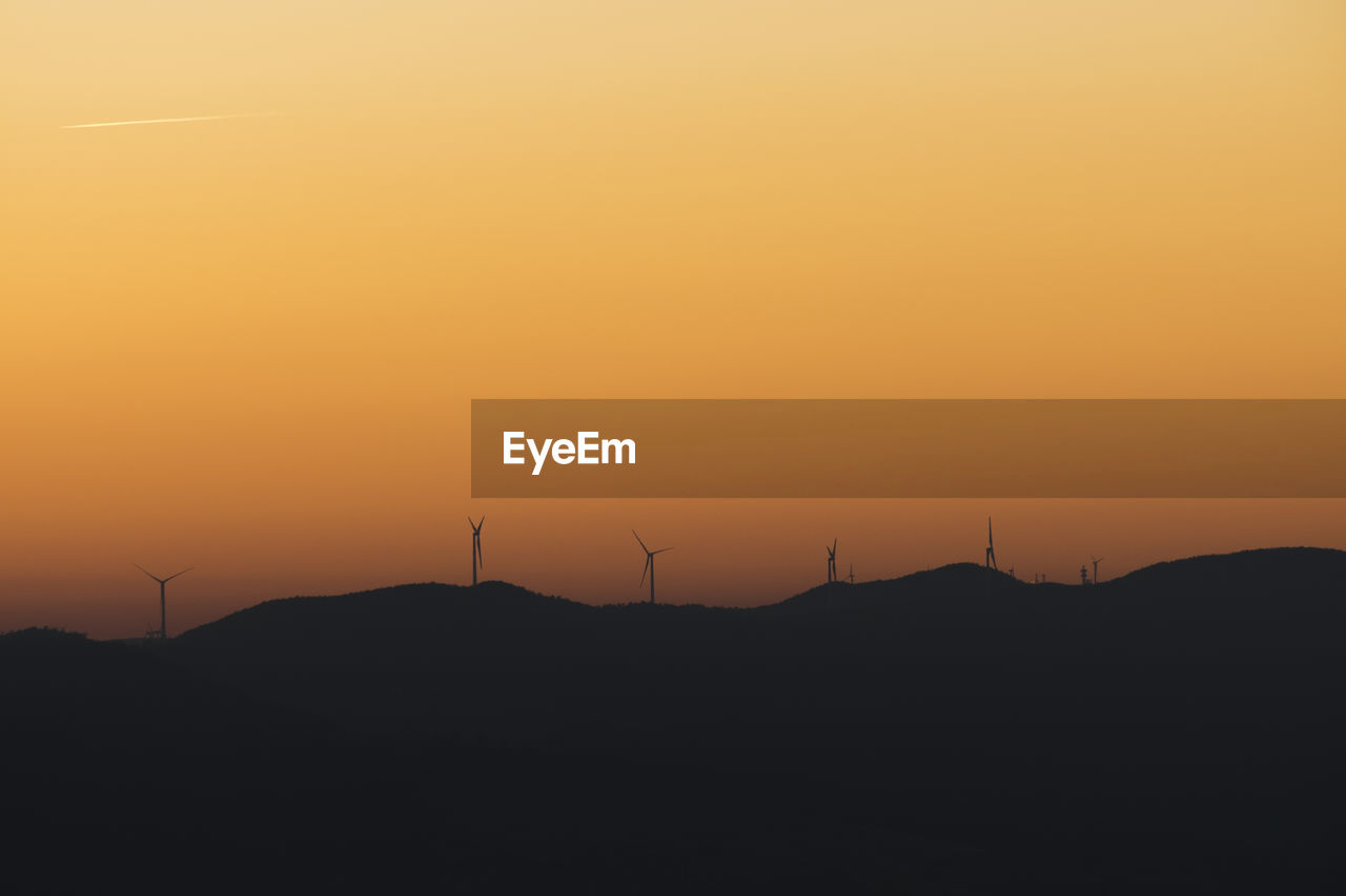 SILHOUETTE OF WIND TURBINE AGAINST ORANGE SKY