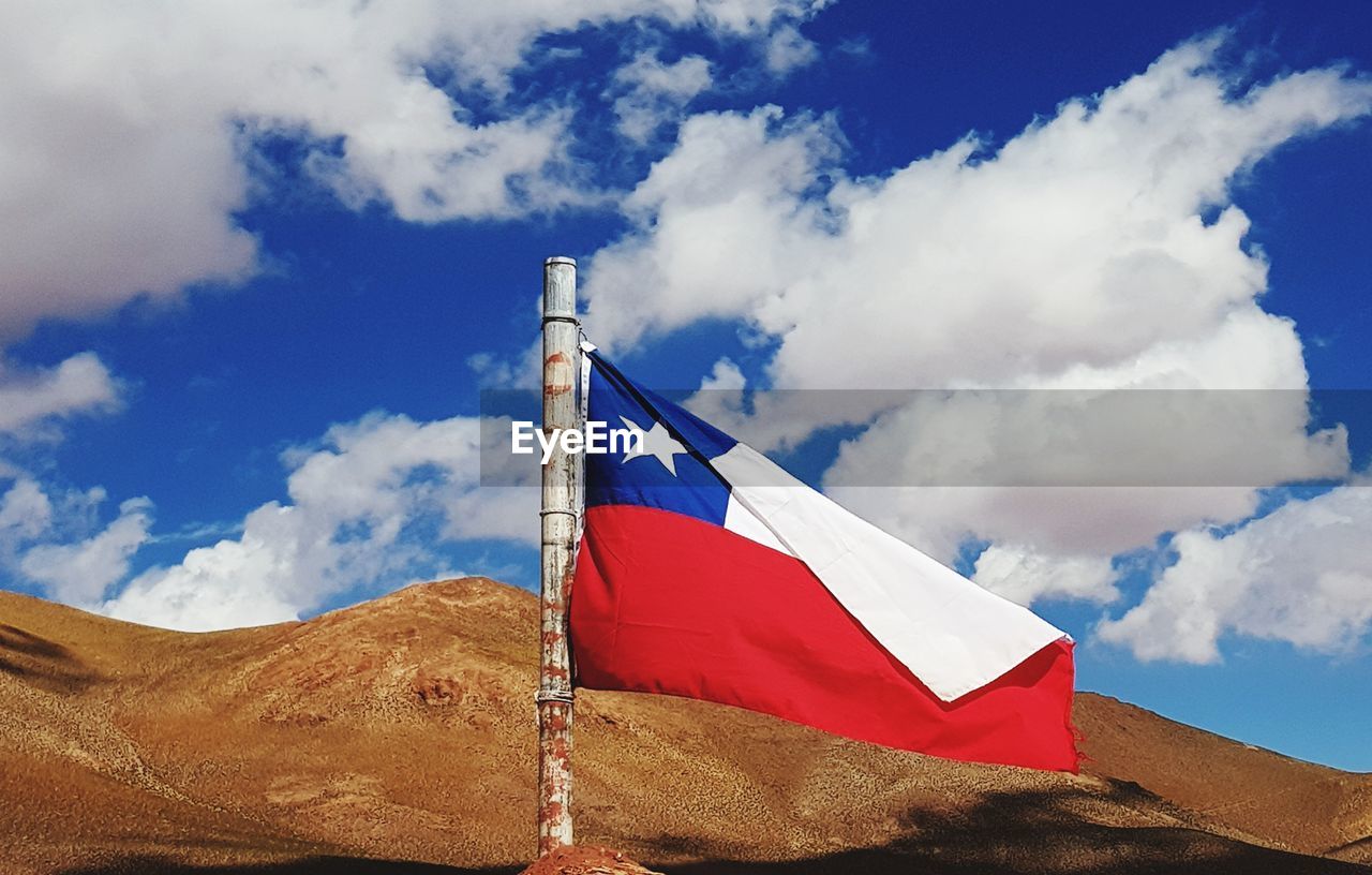 Low angle view of flag of chile on mountain against blue cloudy sky
